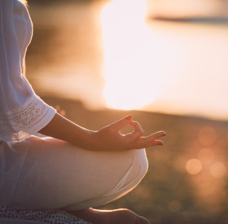 Image of a woman sitting in lotus pose, holding a mudra, surrounded by nature during sunset, symbolizing the practice of Raja Yoga and advanced techniques.
